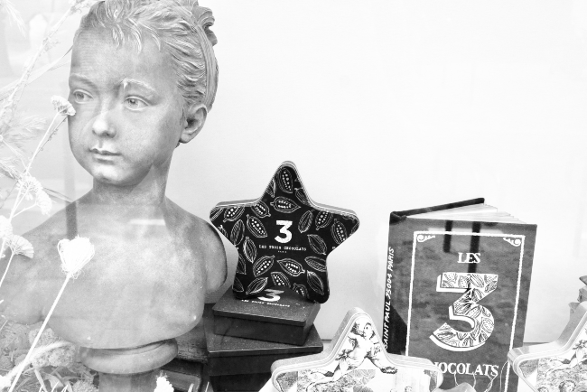 A statue, star shaped box, and book in the Les Trois Chocolats shop window