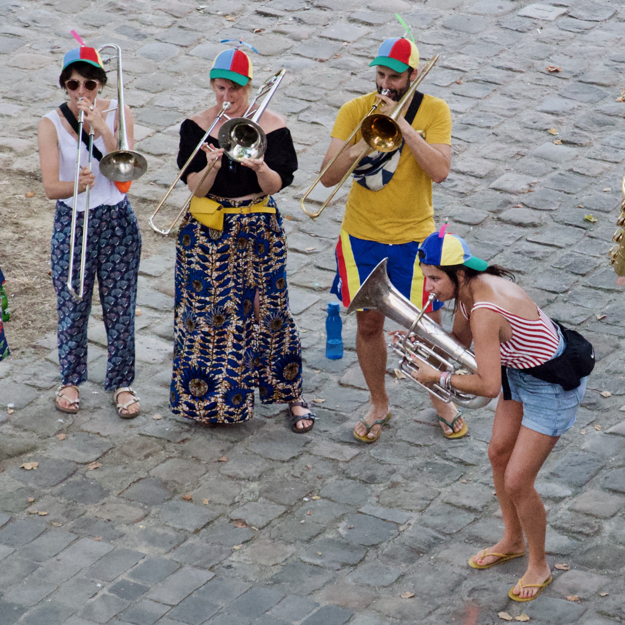 a photo of 4 people playing brass instruments wearing colourful hats with a propeller on top