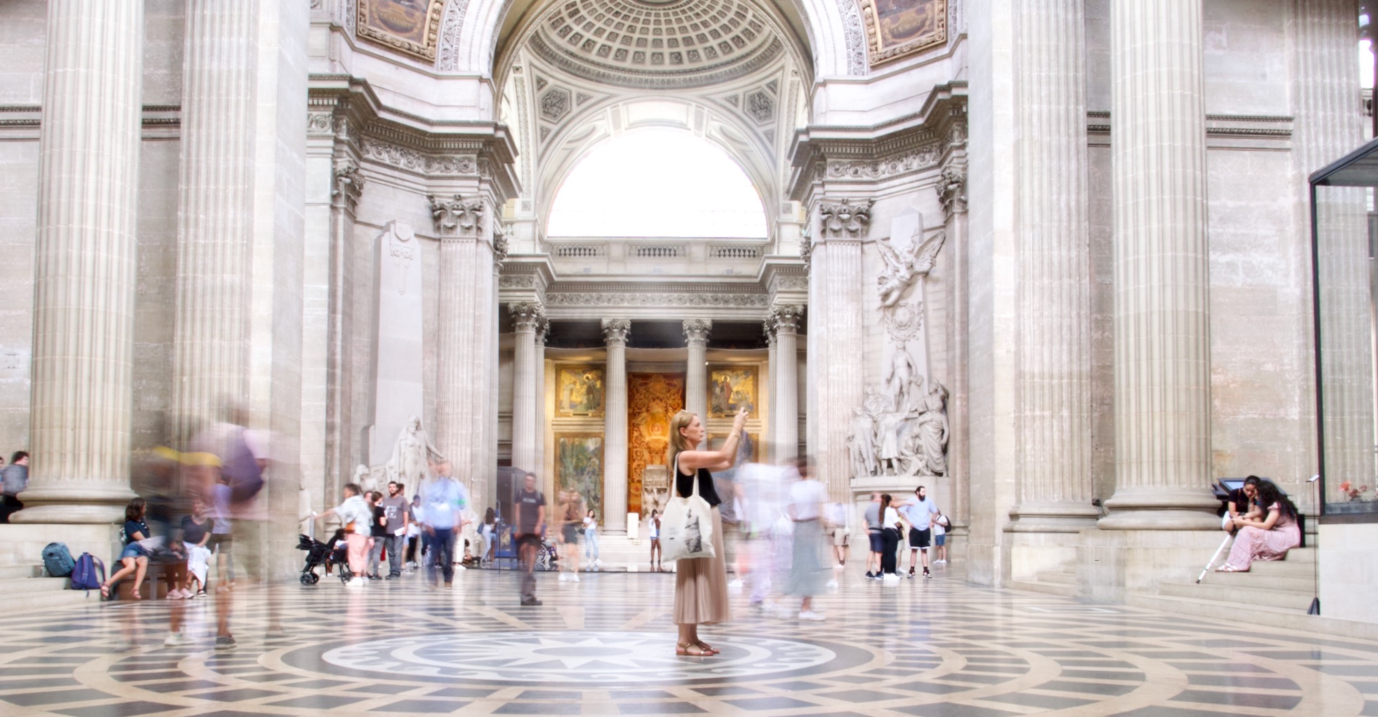 a time lapse photo of a woman in the middle of an impressive building with blurred passers by